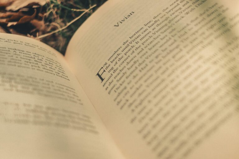 A close-up of an open book page with blurred text, surrounded by leaves, outdoors.