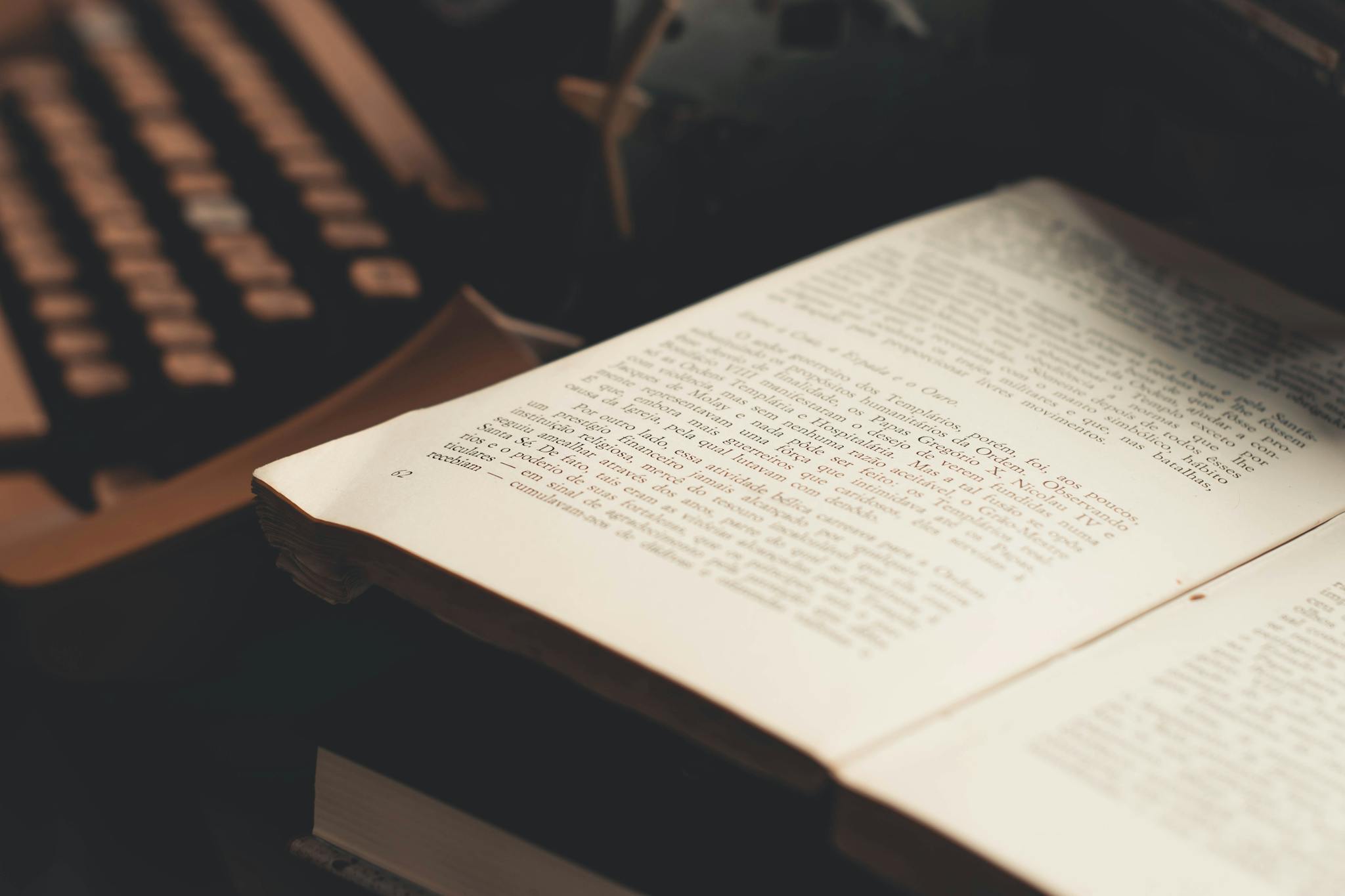 An open book with visible text in front of an antique typewriter, evoking a vintage literary theme.