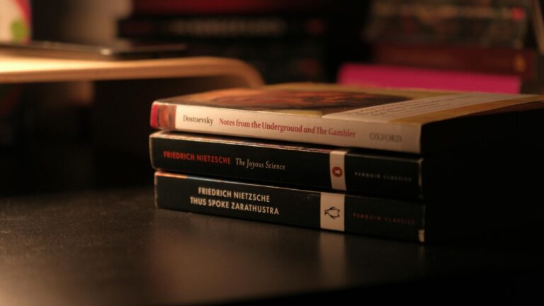 Stack of classic books by Dostoevsky and Nietzsche on a dark desk.